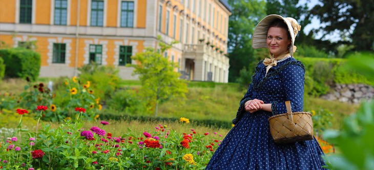 En kvinna i 1800-talsklädsel i trädgården framför Nynäs slott.
